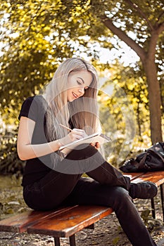 Smiling girl with pencil writing/drawing on notebook in the park