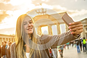 Smiling girl with phone taking selfie photo in front of Brandenburg gate in Berlin