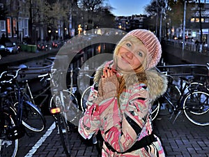 Smiling girl in pink jacket near the canal of Amsterdam on blue hour evening among bikes