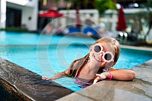 Smiling girl with pink sunglasses enjoys summer pool fun. Child in swimwear hangs on poolside, vacation vibe, kids