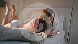 Smiling girl playing mobile phone games online at home. Relaxed teenager typing
