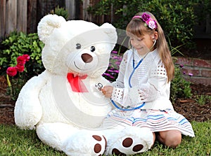 Smiling girl plays the doctor with huge toy white bear