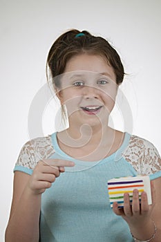 A smiling girl pointing to a sguishy toy cake in her head over light plain background