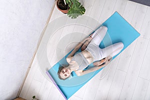 Smiling girl practices yoga at home.Young woman does exercises for stretching and flexibility of joints. Supta Virasana