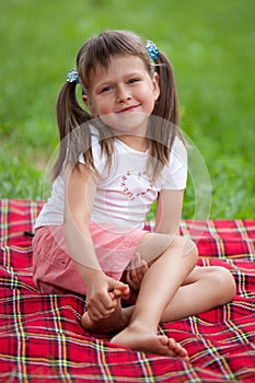 Smiling girl preschooler sitting on plaid in park