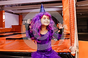 smiling girl in the purple wig and the carnival cap on the trampoline arena