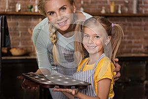 Smiling girl putting with her mother pastry in the oven