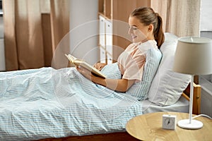 smiling girl reading book in bed at home