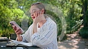 Smiling girl reading message on mobile phone sitting park recreation close up.