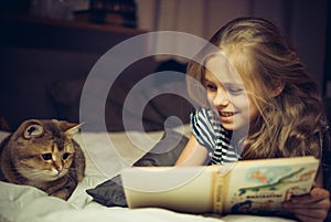 Smiling girl reads book to a cat