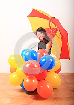 Smiling girl with red and yellow umbrella behind inflating balloons