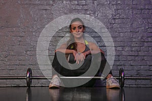 Smiling girl resting at the gym, barbells under her feet