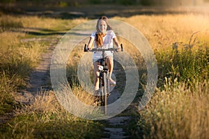 Smiling girl riding on bicycle in meadows at sunset