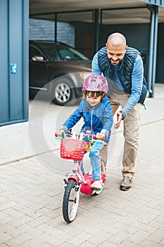 Smiling girl riding a bike with her father's hepl