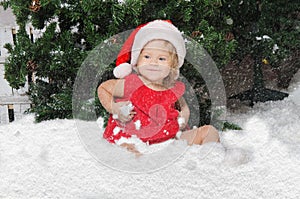 Smiling girl in santa costume sits on snow