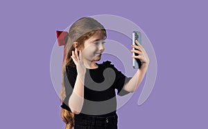 The smiling girl sends greetings to her friends using her mobile phone and social networks, on a purple background.
