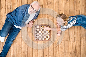 Smiling girl with senior man playing chess on wooden floor