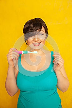 Smiling girl with short hair and a curvy figure stands with a toothbrush in her hands on yellow solid studio background