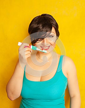 Smiling girl with short hair and a curvy figure stands with a toothbrush in her hands on yellow solid studio background