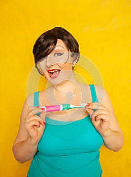 Smiling girl with short hair and a curvy figure stands with a toothbrush in her hands on yellow solid studio background