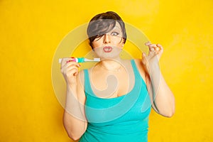 Smiling girl with short hair and a curvy figure stands with a toothbrush in her hands on yellow solid studio background