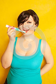 Smiling girl with short hair and a curvy figure stands with a toothbrush in her hands on yellow solid studio background