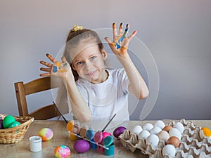 A smiling girl shows her palms covered in paint stained with eggs. Easter. Painted eggs. Multi-colored children\'s lodons.