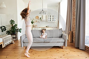 Smiling girl sits on the couch in a bright studio apartment and looks at her mother