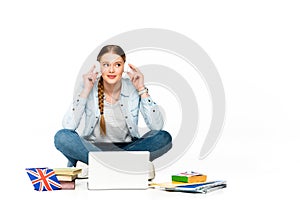 Smiling girl sitting on floor in headphones near laptop, books and copybooks, uk flag