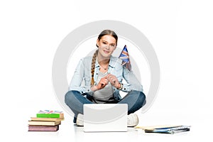 Smiling girl sitting on floor with laptop, books and copybooks and holding uk flag