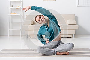 smiling girl sitting in lotus position on yoga mat and stretching