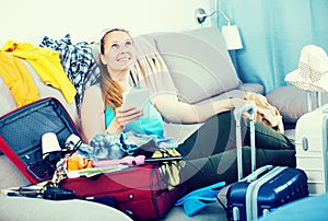 Smiling girl sitting on sofa and packing suitcase