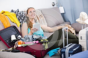 Smiling girl sitting on sofa and packing suitcase