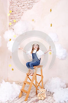 Smiling girl sitting on the stairs in the sky with clouds and with the stars. Little astrologer Little traveler. The girl flies in