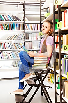 Smiling girl sitting on step ladder in library