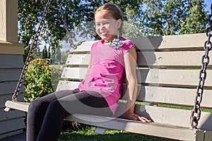 Smiling girl sitting on swing bench in the park