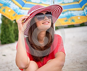 Smiling girl sitting under umbrella on the sand