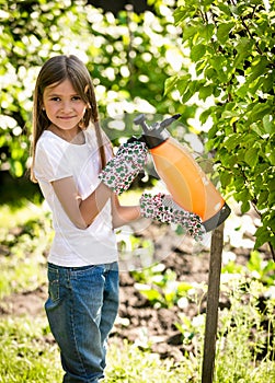 Smiling girl spraying small apple tree with fertilizers