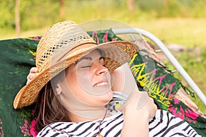 Smiling girl in a straw hat lies on a cot outdoors