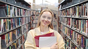 Smiling girl student holding notebooks standing in college library, portrait.