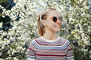 Smiling girl in sunglasses on background of blossoming apple tree