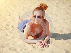 Smiling girl in sunglasses lies on the sand on a summer sunny day. Beach vacation