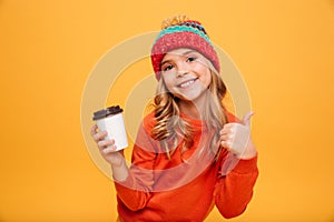 Smiling girl in sweater and hat holding cup of tea