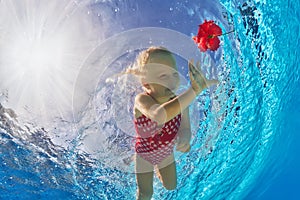 Smiling girl swimming underwater in pool for tropical red flower