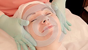 Smiling girl takes a facial massage in a beauty salon. Masseur kneads the girl`s ears. Beauty and health. Close-up of female face