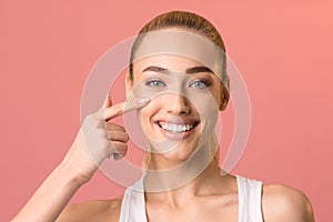 Smiling girl touching face applying facial cream posing in studio