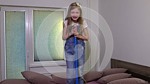 Smiling girl with toy microphone dancing and singing in the bed
