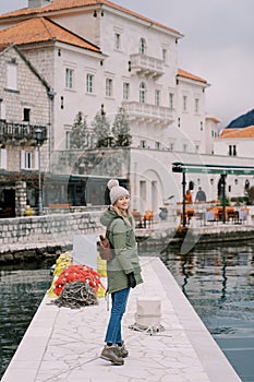 Smiling girl-traveler stands on the pier against the backdrop of the old house of Perast. Montenegro