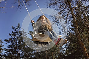 Smiling girl with tresses hair in grey coat flying on a swing against blue sky