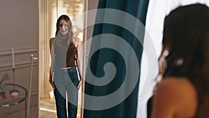 Smiling girl trying large jeans looking mirror. Happy young woman jump admiring